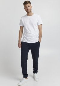 White crew-neck t-shirt, dark blue jogger pants with elastic cuffs, paired with white sneakers. Simple design, minimalistic style.