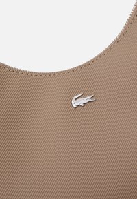 Haut de sport en tissu texturé marron avec un col rond, présentant un petit logo crocodile argenté à l'avant.