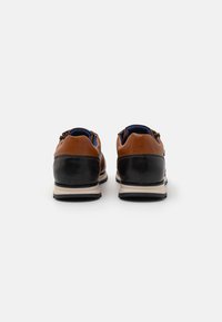 Scarpe in pelle marrone e nera con una forma arrotondata, caratterizzate da un tacco a contrasto e una suola texturizzata. Dettaglio con zip sul retro.