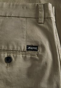 Pantalones caqui hechos de tela tejida, con cierre de botón, un bolsillo trasero con etiqueta y una sutil textura diagonal.