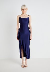 Satijnen marineblauwe jurk met een gestructureerde, aansluitende corsage, dunne bandjes en een gerimpeld detail aan de zijkant, met een hoge split tot boven de dij en een gladde textuur.