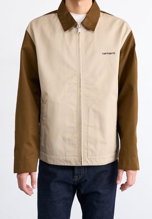 Beige en bruine ritsjack met een contrasterende kraag en mouwen; gemaakt van een gladde stof met het logo op de borst.