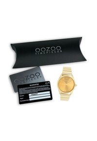 Montre en métal doré avec un cadran rond, un cadran à rayures verticales et un bracelet à maillons. Accompagnée d'une boîte noire et d'une carte de garantie.