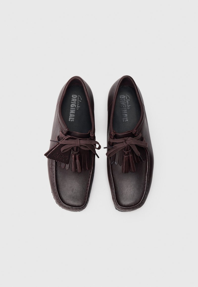 Brown leather shoes with a rounded toe, featuring a lace-up design with tassels, and textured accents. The interior has a padded black lining.