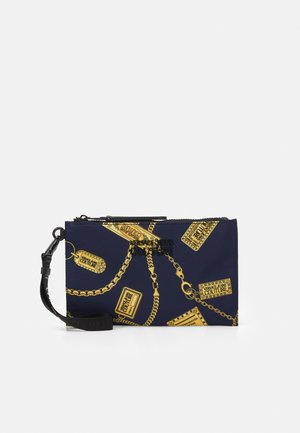 Marineblaue Wristlet-Tasche mit goldenen Ketten- und Etikettenmustern, schwarzem Reißverschluss und abnehmbarem Handgelenksriemen.