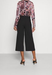 Zwarte cropped wide-leg broek met een gladde textuur. Gecombineerd met een langemouwtop in een meerkleurenpatroon met geometrische en bloemmotieven.