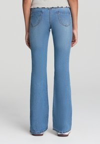 Jeans a campana blu chiaro con una texture denim classica, dotati di due tasche posteriori e un sottile motivo sbiadito lungo le gambe.