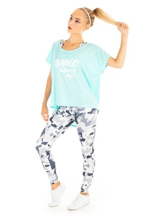 Light blue oversized t-shirt with white text, paired with gray camouflage leggings. Model wears white sneakers and has long hair tied back.