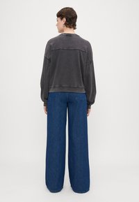 Sudadera recortada gris con una textura suave, combinada con jeans de mezclilla azul de pierna ancha. Las características notables incluyen hombros caídos y costuras en contraste.
