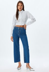 Camisa recortada de rayas blancas y azules con botones al frente, combinada con jeans de mezclilla azul de tiro alto y pierna ancha con dobladillos deshilachados.