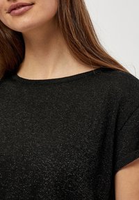 Černý pletený top s volným střihem, kulatým výstřihem a krátkými rukávy, který obsahuje jemné metalické vlákna pro texturovaný vzhled.