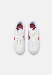 Hvite Nike-sneakers med røde detaljer og logo, med en glatt overdeler, polstret innside og tradisjonell snøring.