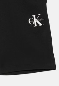 Black cotton shorts featuring a smooth texture, with a white "CK" logo printed on the left leg and finished with a clean hem.