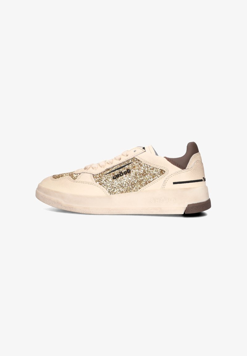 Sneaker met bovenwerk van crème leer, gouden glitteraccenten aan de zijkanten, bruine hielstuk, gestructureerde zool en zwarte strepen nabij de veters.