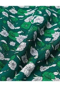Tissu vert avec un motif floral composé de fleurs blanches et vertes ainsi que des tiges et feuilles contournées en noir, présenté avec de douces pliures.
