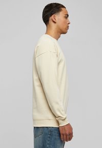 Light beige sweatshirt made of soft fabric, featuring a crew neckline, long sleeves, ribbed cuffs, and a relaxed fit. Paired with blue jeans.