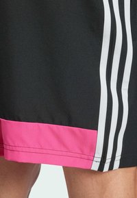 Pantalones cortos atléticos negros con un dobladillo de canalé rosa y acentos de rayas blancas. Hechos de una tela suave con un corte recto.