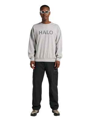 Mand iført grå "HALO" sweatshirt, sorte cargobukser, beige og sorte sneakers og hvide sporty solbriller, stående mod hvid baggrund.