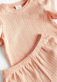 Set de top și pantaloni scurți tricotat de culoare piersiciu, cu un model texturat ce include dungi subtile și mici găuri, talie elastică la pantaloni.
