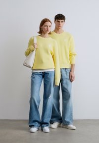 Κίτρινα πουλόβερ με ραβδώσεις, λευκές λεπτομέρειες, ζευγαρωμένα με ανοιχτό μπλε τζιν παντελόνια με φαρδιά μπατζάκια και λευκά αθλητικά παπούτσια. Λείο ύφασμα και άνετη εφαρμογή.