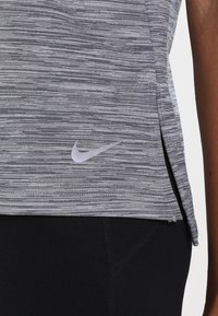 Top atlético gris con un patrón texturizado a rayas; presenta un pequeño logotipo blanco de Nike en la parte inferior izquierda. Tiene pequeñas aberturas laterales cerca del dobladillo.