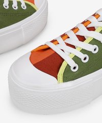 Colorful canvas sneakers featuring green, orange, and red panels with white rubber soles and eyelets. Textured fabric and flat laces.