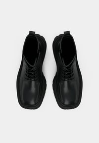 Black leather ankle boots with a smooth finish, round toe, and six eyelets. Thick rubber sole with a slight tread pattern for stability.