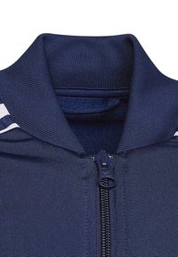 Navy zip-up jacket featuring a high collar, textured fabric, and a contrasting white stripe along the shoulder, with a sturdy zipper closure.