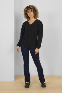 Maglione nero a maglia con scollo a V e motivo testurizzato, abbinato a jeans blu scuro aderenti e calzature nere con accenti dorati.