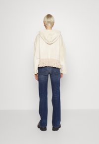 Sudadera color crema con un dobladillo con flecos, combinada con jeans acampanados azules. La sudadera tiene una textura suave y un corte relajado.