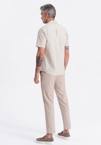 Hellbeige Kurzarmhemd mit einem Rückenfalten, kombiniert mit hellbraunen Slim-Fit-Hosen und braunen Slippern. Glatte, lässige Stoffe.