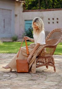 Hnědá kožená crossbody taška s hladkým povrchem, obdélníkovým tvarem a nastavitelným popruhem. Má přední kapsu a jemný detail loga.