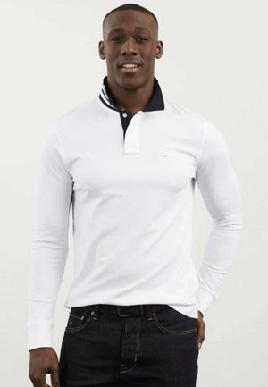 Polo shirt blanc à manches longues avec col et bordure marine, doté d'une patte de boutonnage à trois boutons et d'un petit logo sur la poitrine gauche.