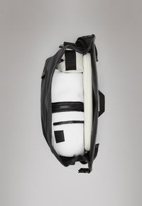Saco de nylon preto com interior em lã branca, apresentando bolsos com fecho éclair, alças ajustáveis e uma etiqueta em tom castanho. Vista aberta.