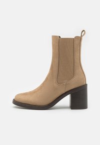 Tan suede ankle boot with elastic side panels, rounded toe, and a textured block heel. Minimalist design with clean lines.