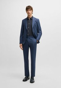 Granatowy garnitur o dopasowanym kroju, z fakturowanej tkaniny, zestawiony z czarną koszulą w kropki i czarnymi butami eleganckimi. Prosty, nowoczesny design.