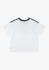 Balta T-krekls ar apaļu tumši zilu apkakli un tumši zilām svītrām uz pleciem. Izgatavots no kokvilnas, ar īsām piedurknēm un taisnu apakšmalu.