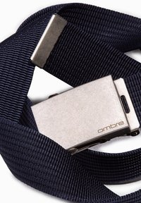 Marineblå stofbælte med en sølvfarvet, rektangulær metalspænde med et præget brandnavn. Bæltet har en struktureret, v�ævet overflade.