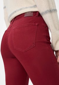 Bordeauxfarbene Jeans aus Denim mit schmalem Schnitt, ausgestattet mit Gesäßtaschen, dezenten Stickdetails und einem markierten Lederpatch am Bund.