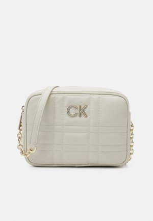 Bolso bandolera rectangular de cuero crema con costuras acolchadas, logo CK dorado en el frente y cadena dorada con almohadilla de cuero en el hombro.