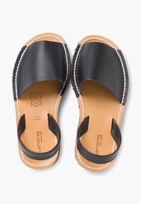 Sandali in pelle nera con design open toe, accentuati da cuciture bianche, dotati di un cinturino posteriore e di una soletta marrone.