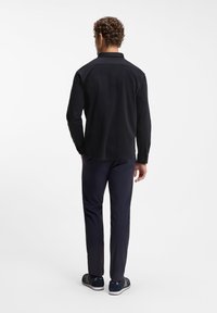 Μαύρο πουκάμισο με μακριά μανίκια και γιακά, συνδυασμένο με ναυτικό μπλε παντελόνι και ναυτικά μπλε αθλητικά παπούτσια, που δείχνει ομαλή υφή και εφαρμοστή γραμμή από την πίσω όψη.