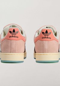 Buty sportowe Adidas z różowym zamszowym obcasem, czarnymi siateczkowymi panelami bocznymi, białą wyściółką, kremową podeszwą środkową i niebiesko-zieloną gumową podeszwą zewnętrzną.