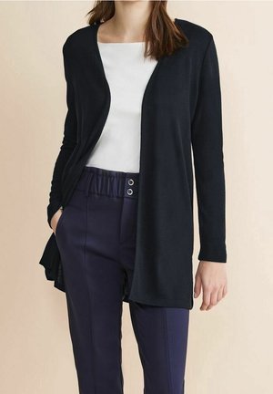 Cardigan nero in tessuto morbido, design aperto davanti, maniche lunghe, abbinato a pantaloni blu navy. Texture con finitura liscia e senza chiusure.