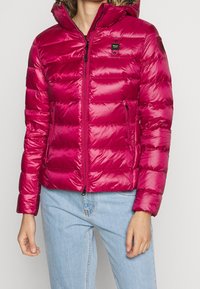 Doudoune fuchsia à finition brillante, poches zippées, capuche amovible et design matelassé horizontal ; tissu léger et doux au toucher.