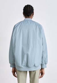 Svetlo modrá bomber bunda s voľným strihom, elastickými manžetami a lemom, hladkým materiálom a jednoduchým dizajnom. Žiadne viditeľné kovania ani vzory.