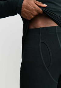 Fekete leggings puha tapintású anyagból, rugalmas derékpánttal. Kör alakú nyílással és kontrasztos varrással díszítve.