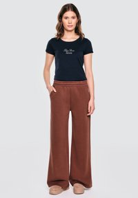 Námornícky tričko s textem "Big Star Jeans", v kombinaci s hnědými širokými kalhotami a béžovou obuví; hladký materiál a detaily elastického pásu.