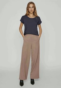 Marineblå kortærmet top kombineret med beige bukser med vide ben, der har sidelommer og en glat tekstur. Bæres med sorte ankelstøvler.