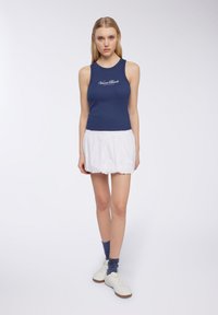 Top senza maniche blu navy con la scritta "Venice Beach", abbinato a una mini gonna bianca plissettata. Completato con calze blu e sneakers bianche.